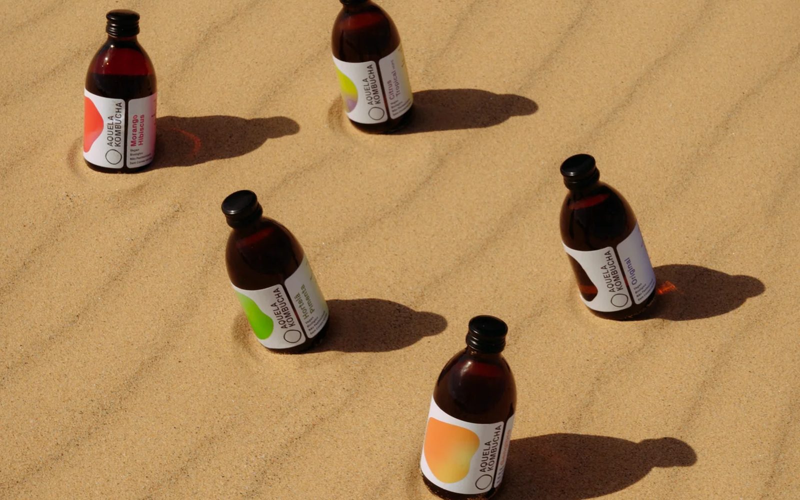 Cinco garrafas Aquela Kombucha de 25 cl numa duna de areia